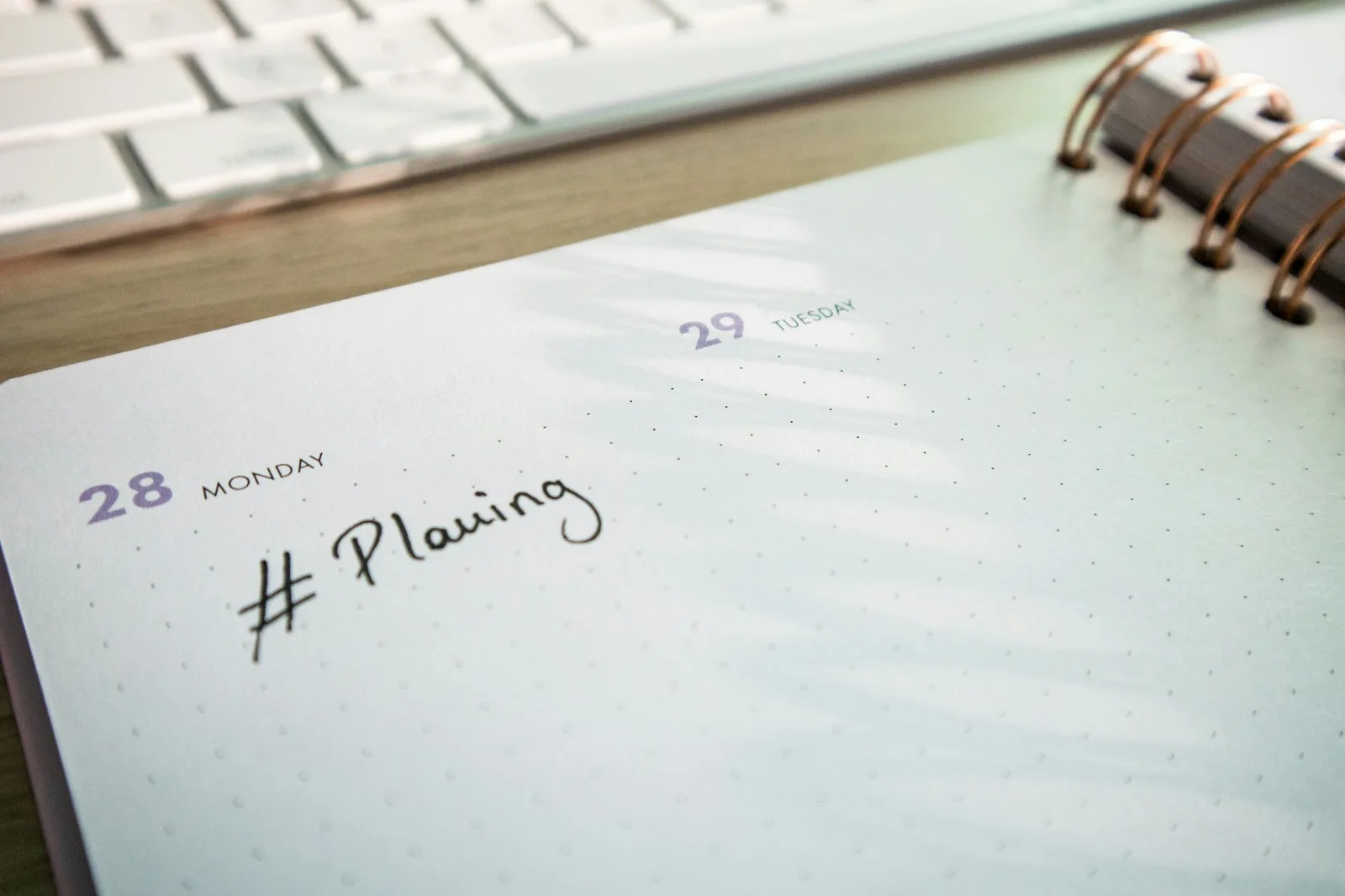 Notepad and physical shift planner on a wooden desk next to a keyboard, representing scheduler coverage planning