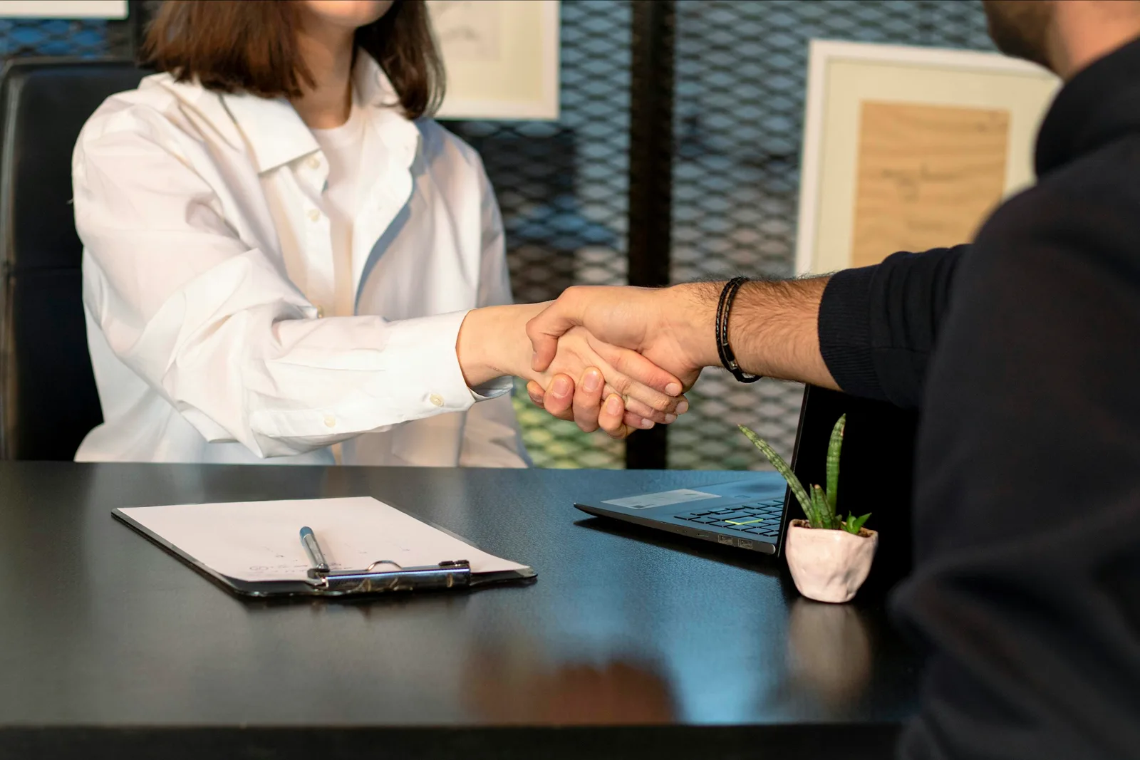 Two people shaking hands during a hiring meeting in front of a laptop