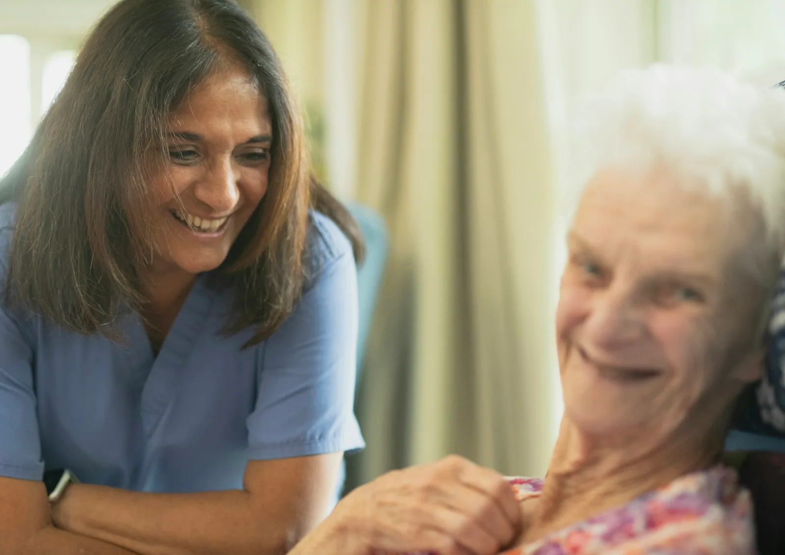 Home care nurse smiling with elderly patient in a sunlit room