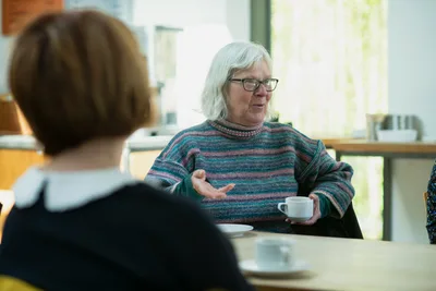 Two women seated across a table from each other, one older and one younger, sharing conversation over coffee