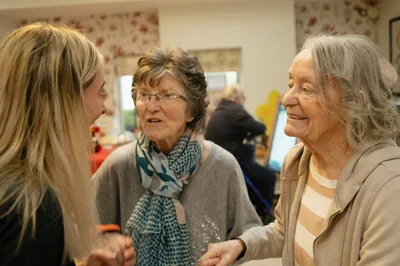 Three women of different ages talking and smiling together in a warmly lit home room