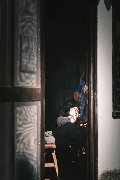Elderly person sitting alone in a doorway, looking outward in quiet solitude