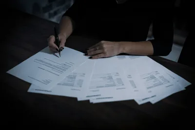 Woman sitting at a desk covered in papers and documents, reviewing paperwork in a professional office