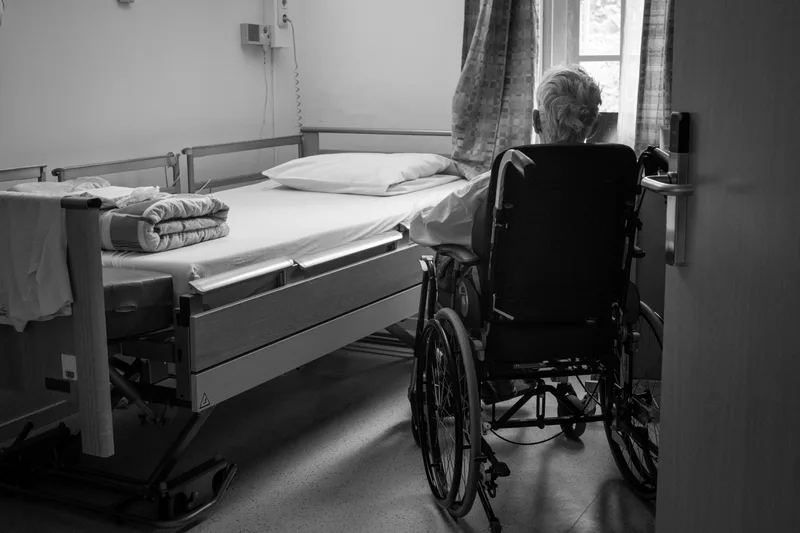 Person sitting in a manual wheelchair positioned near a window inside a home room