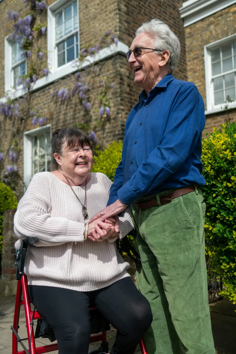 Older man and younger woman standing outdoors together, smiling, in an informal caregiver-client moment