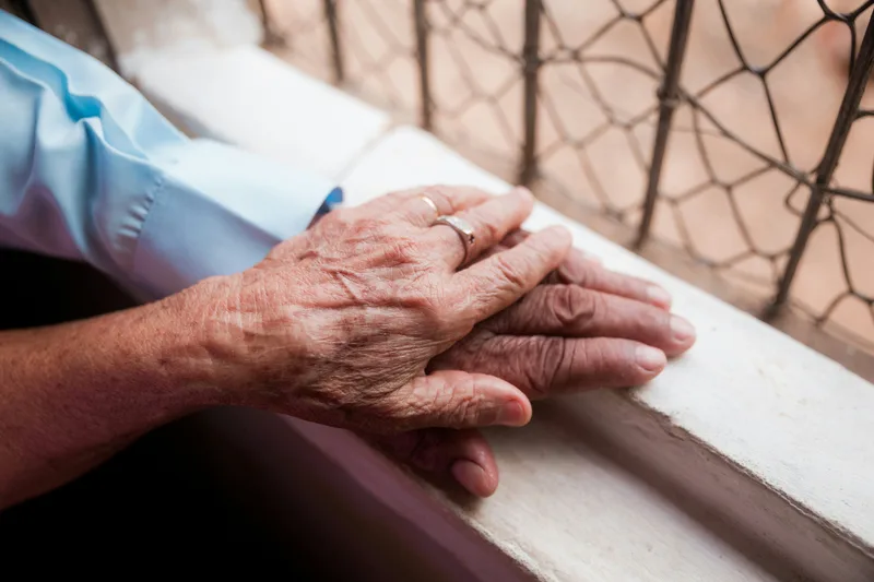 Close-up of an elderly person's hand being held by a younger person's hand against a white background