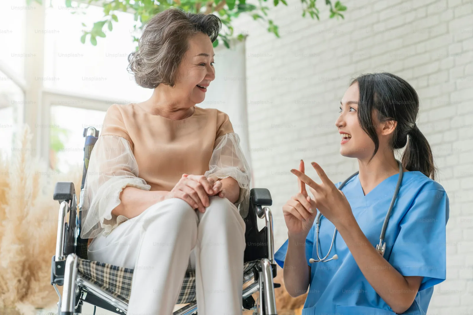 A caregiver in a uniform supports an elderly patient seated in a wheelchair