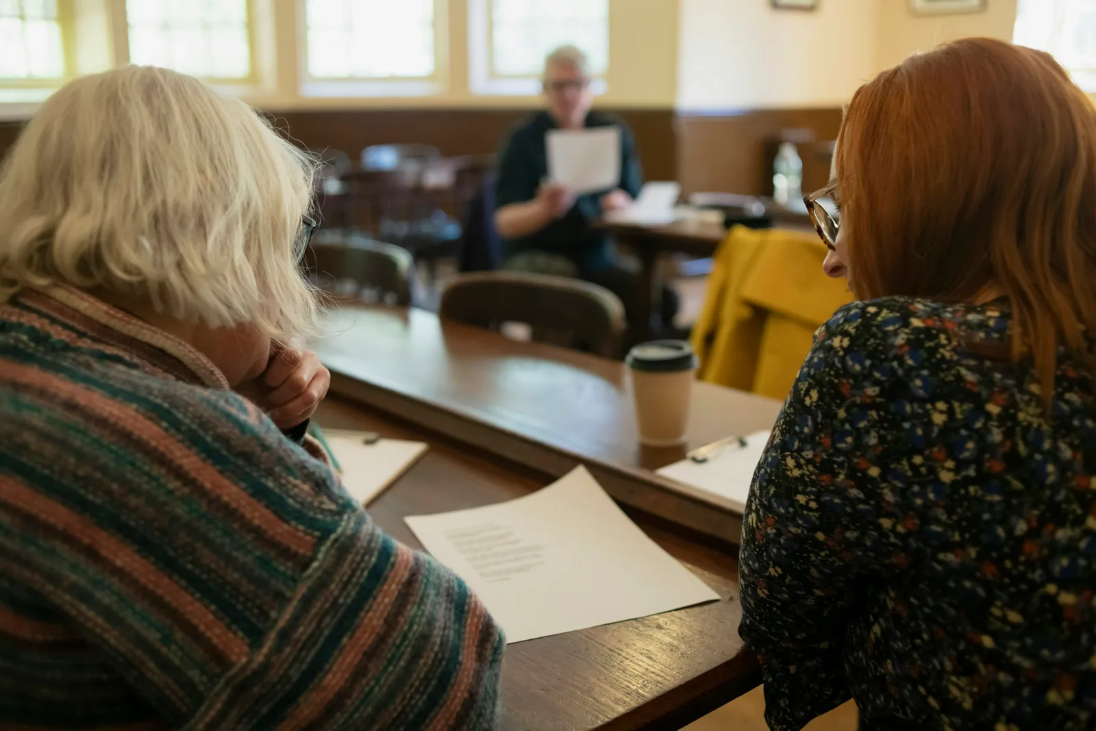 Two women sit at a table reviewing paperwork together, planning care for a family member