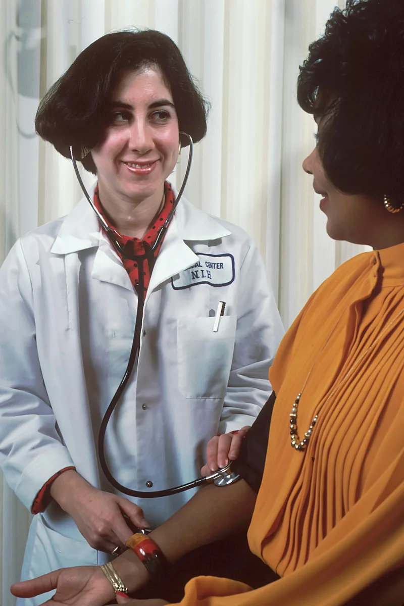 A woman wearing a white doctor's coat facing another woman during a one-on-one conversation in a healthcare office