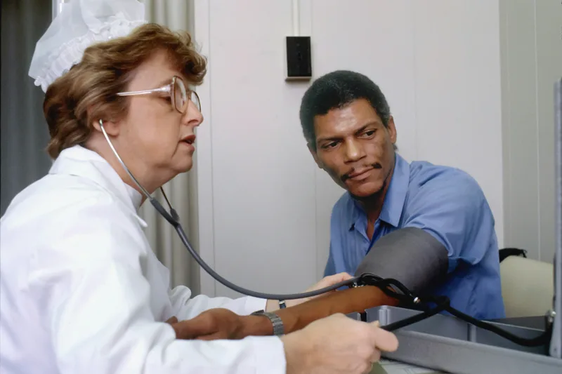 A medical professional holding a stethoscope to the chest of a patient who is seated, performing a health assessment