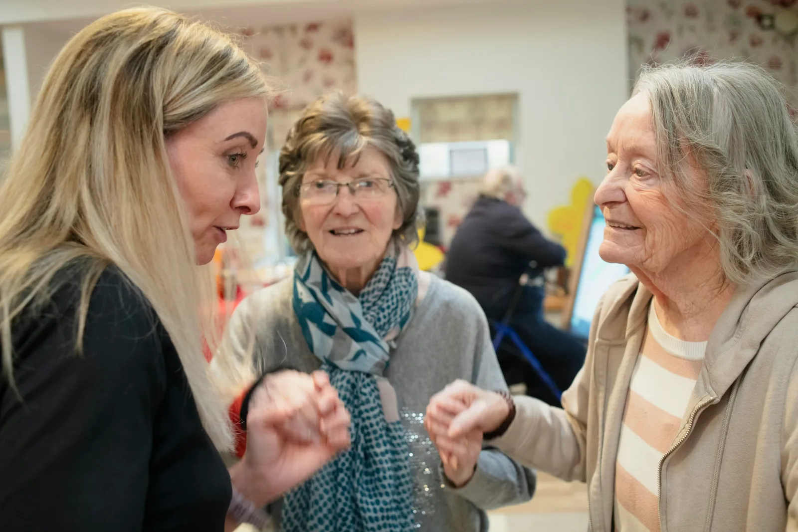 A caregiver speaking with two senior women in a softly lit home setting