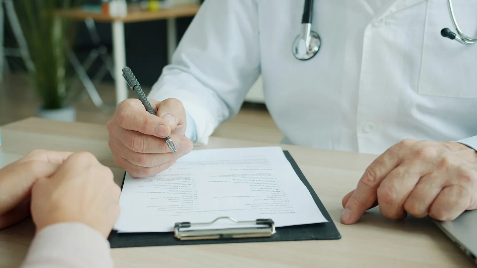 A clinician writing notes on a patient chart at a clinic desk