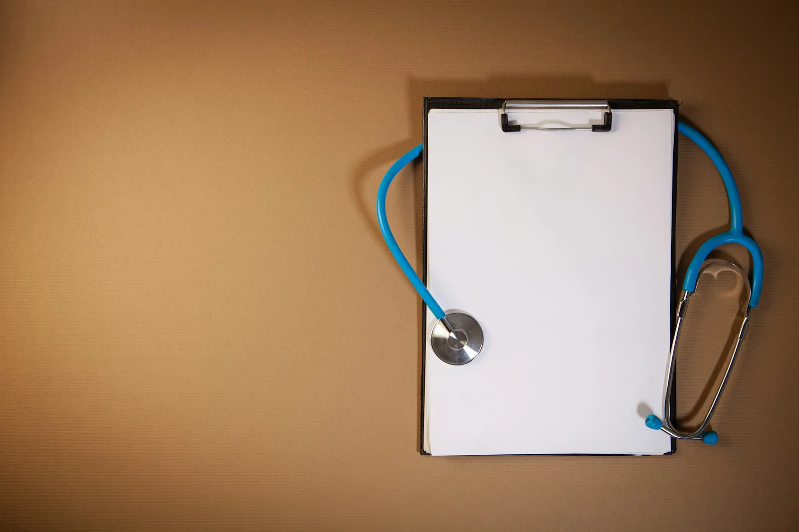 A clipboard with a stethoscope and printed records resting on a wooden background