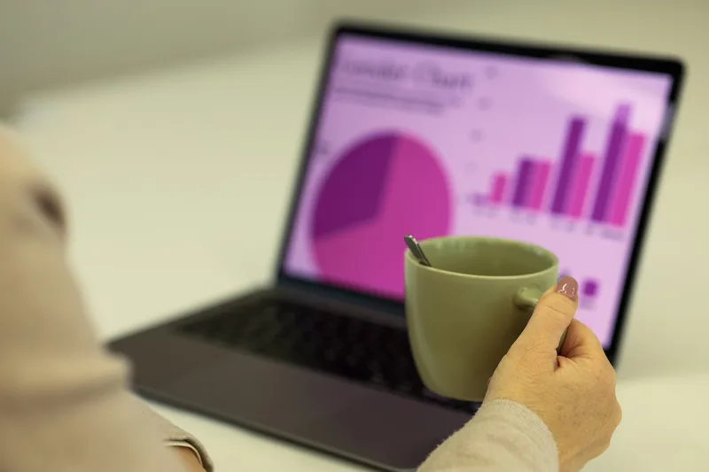 Person working at a laptop with a cup of coffee on the desk, reviewing business data in a workspace