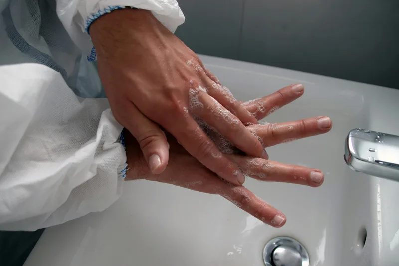Close-up of a person's hands being washed over a white ceramic sink, a standard infection control practice