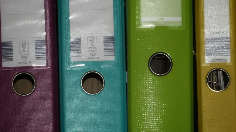 A row of multicolored ring binders arranged in order on a shelf, illustrating an organized document storage and filing system