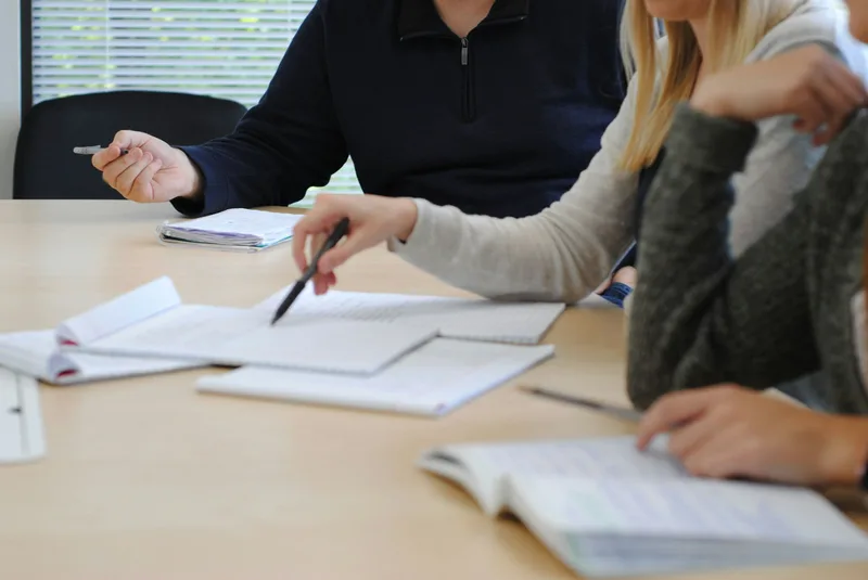 Small group of people seated around a table collaboratively reviewing papers and documents during a work meeting