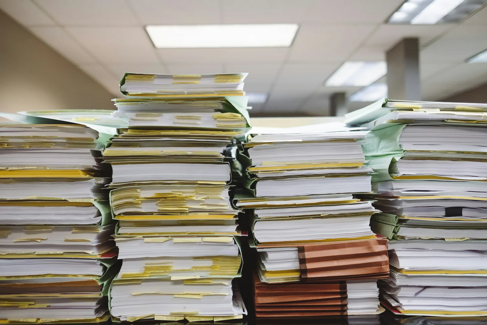 Multiple stacks of white paper documents and brown manila file folders arranged on a flat surface