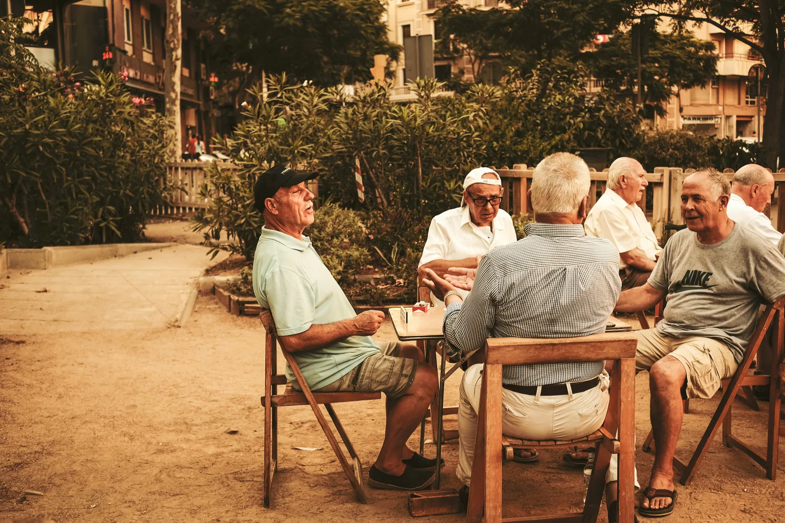 Group of older men seated around a table outdoors, talking and socializing together