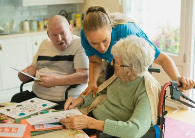 Caregiver assisting an elderly couple with a coloring activity at a table