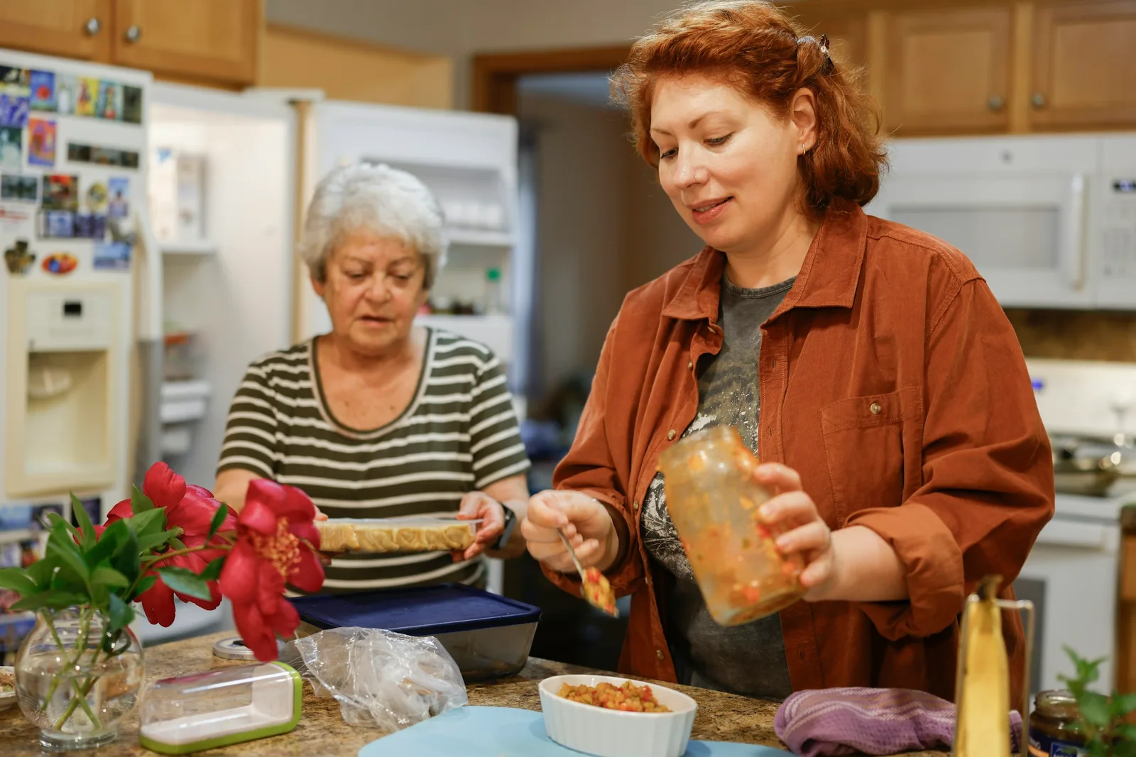 An adult daughter and her elderly mother preparing food together at a home kitchen counter.