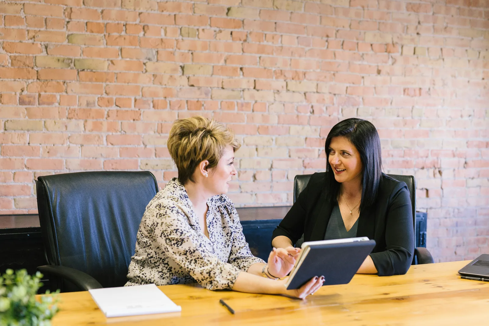 Two women in a professional consultation meeting seated across from each other at a table with documents