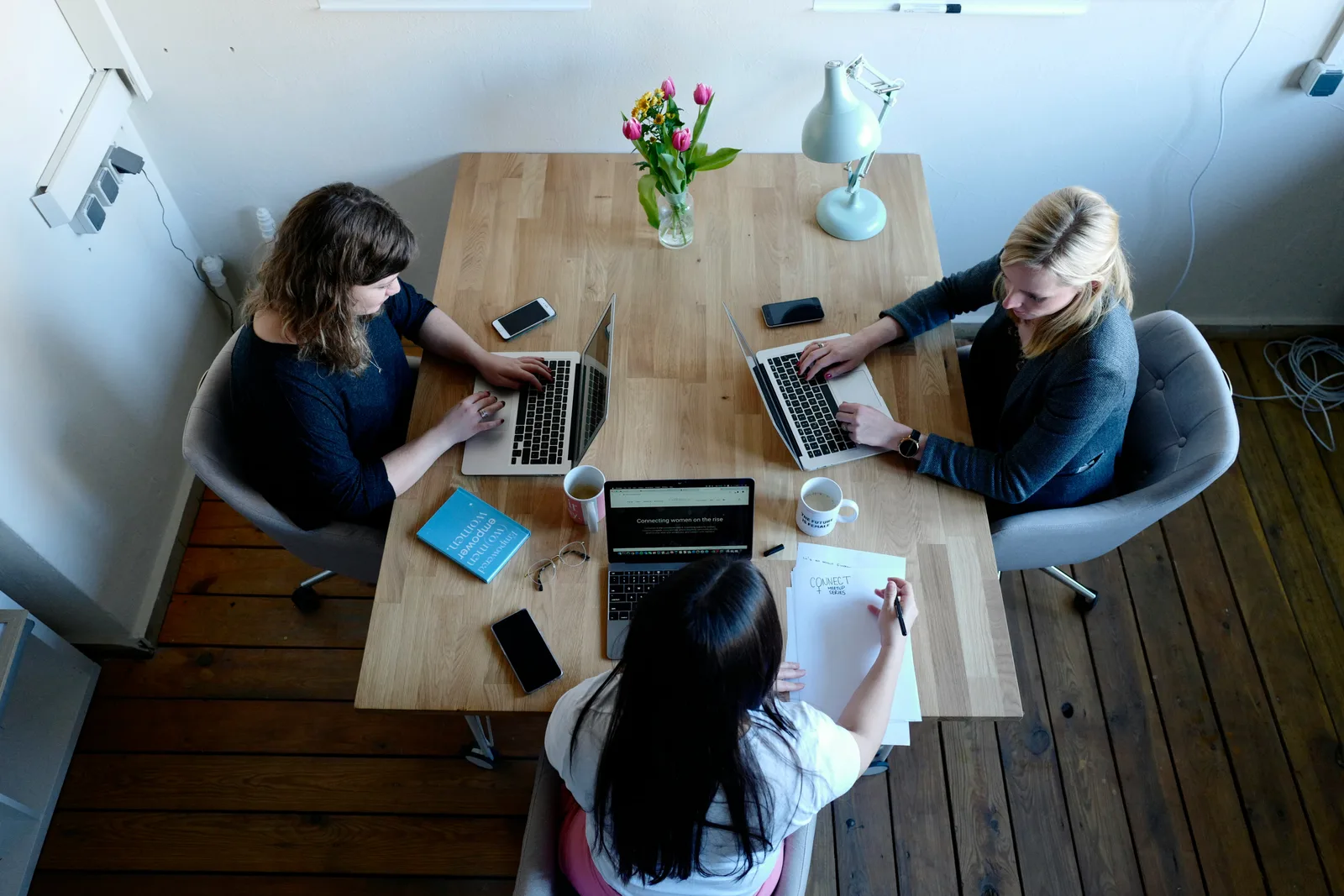 Three women sitting around an office table each working on their own laptop computers