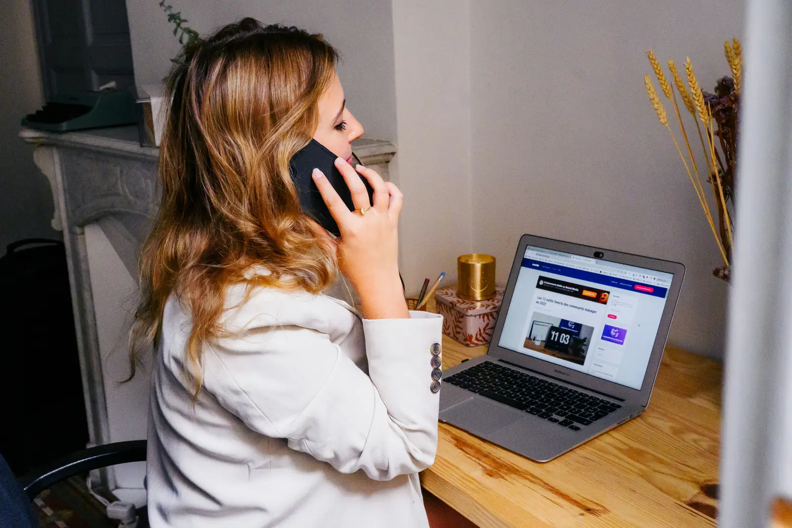 Woman seated at an office desk working on a laptop with a desk phone beside her