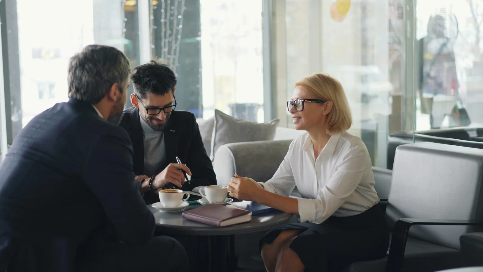 Two men and a woman seated at a conference table engaged in a business conversation with papers in front of them