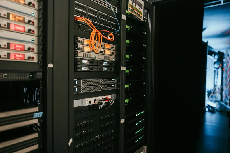 A rack of black server units with blinking indicator lights mounted in a dark server room, viewed from the front