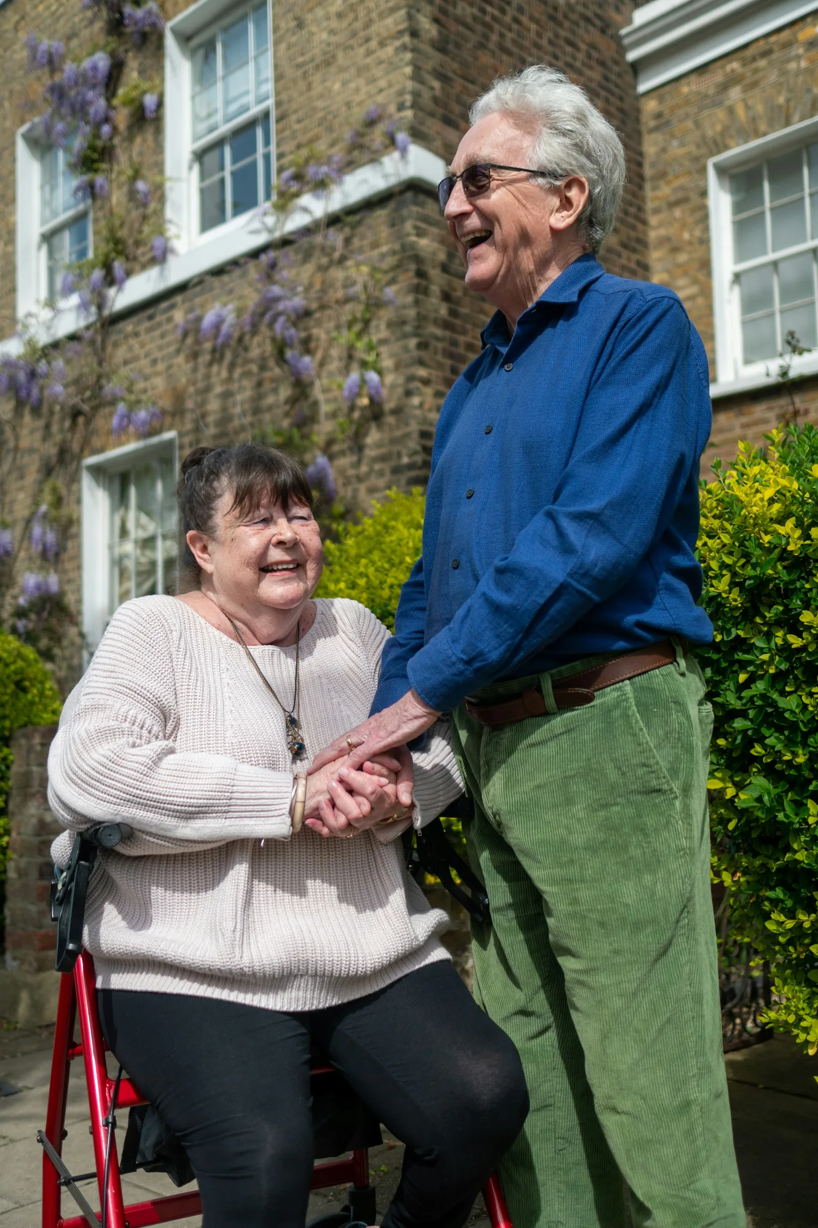 Two adults standing outside a building speaking together, one writing on a clipboard