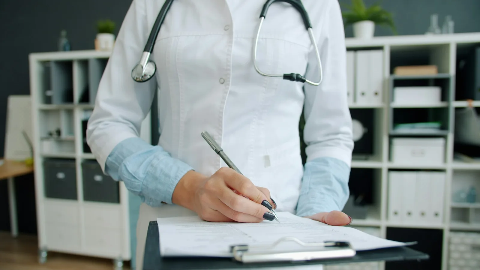 Healthcare professional in white coat writing on a clipboard in an office setting