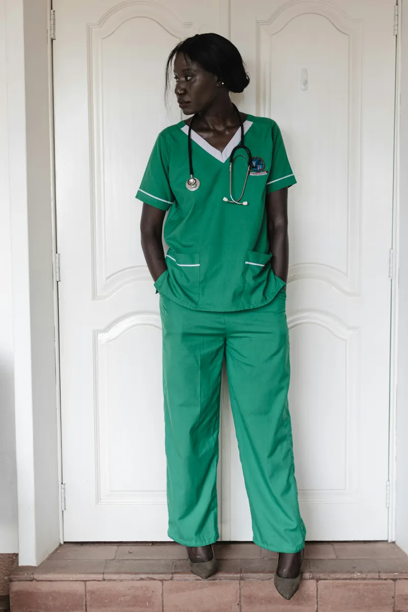 A woman wearing green medical scrubs and a stethoscope standing in a clinical environment