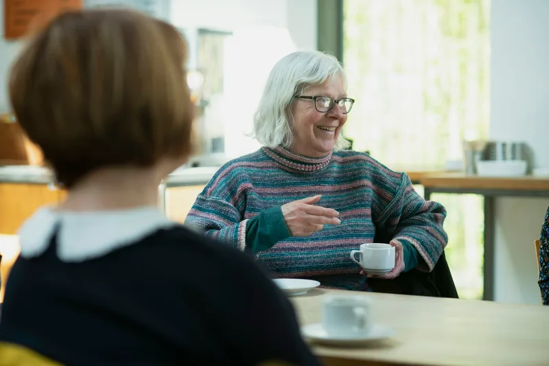 Two women seated at a table across from each other having a focused conversation over coffee
