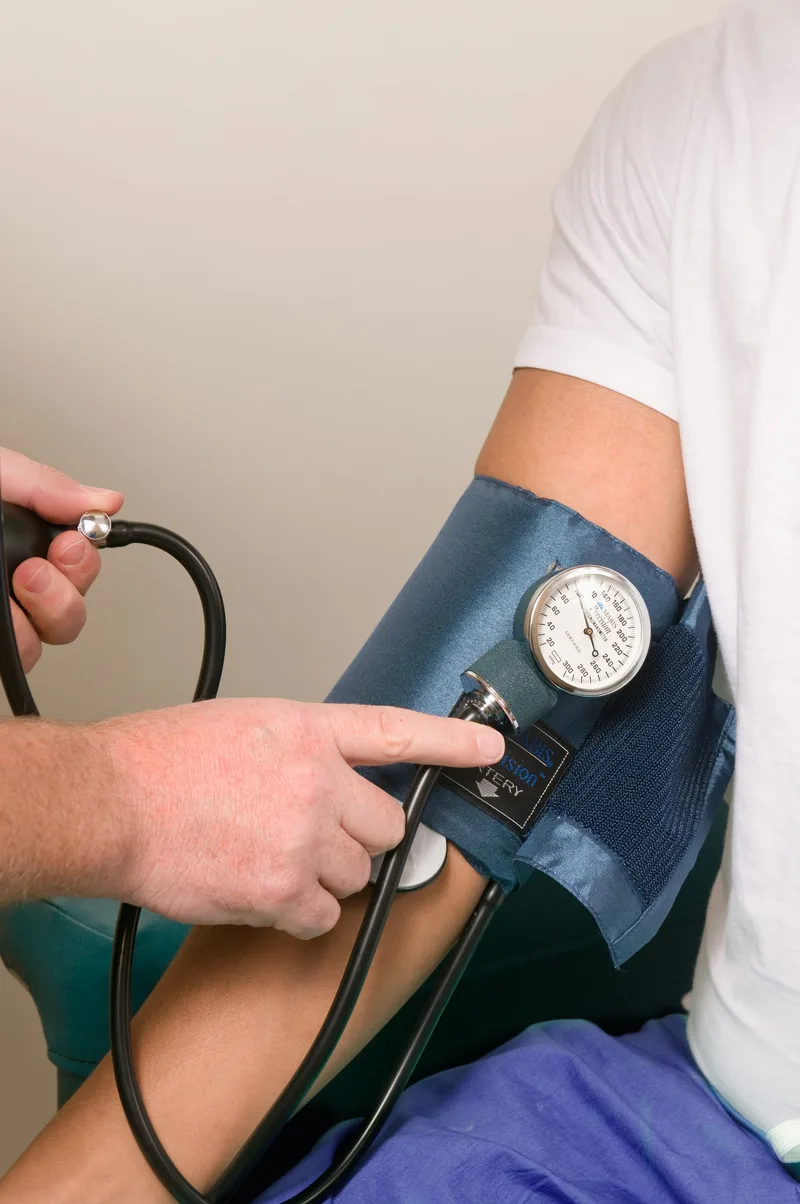 A healthcare worker using a sphygmomanometer to check a patient's blood pressure during a home visit