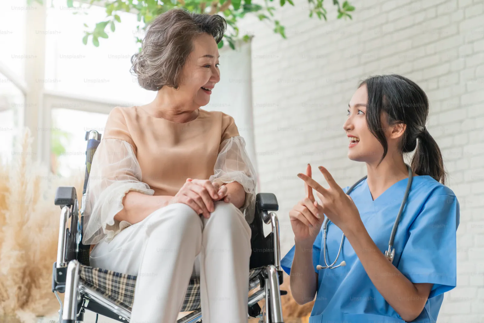 Young caregiver pushing an elderly patient in a wheelchair down a sunlit hallway, both smiling